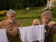 Elderly man and teenage boy joyfully hanging laundry in a sunny garden setting.
