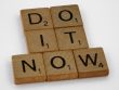 Wooden scrabble tiles forming 'DO IT NOW' on a minimal white backdrop. Inspiring concept.