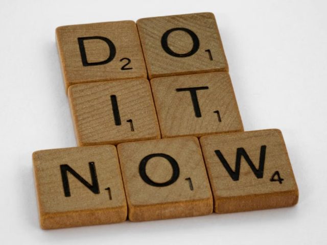 Wooden scrabble tiles forming 'DO IT NOW' on a minimal white backdrop. Inspiring concept.